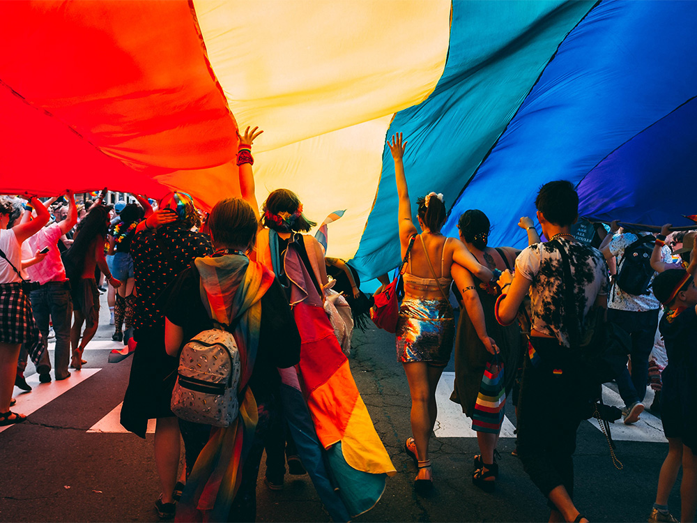 People walking under a large Pride flag