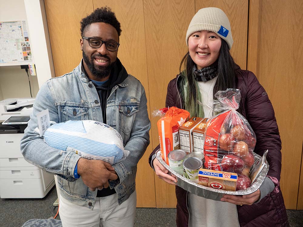 Two people holding a frozen turkey and tray of donated food