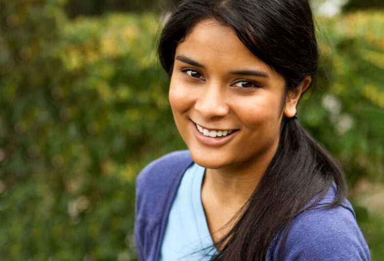 Portait of smiling teen looking at camera against a green bokeh vegetation