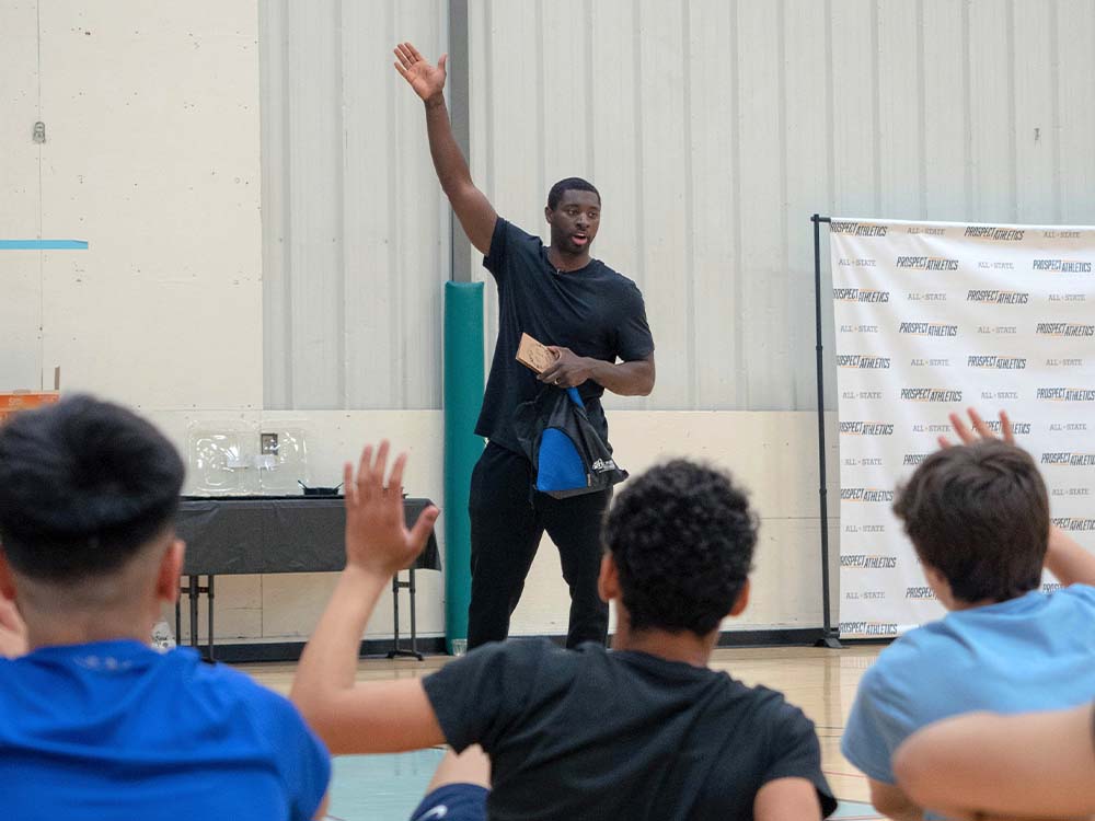 Man speaking in front of a crowd of teens, in a gym, with their hands raised