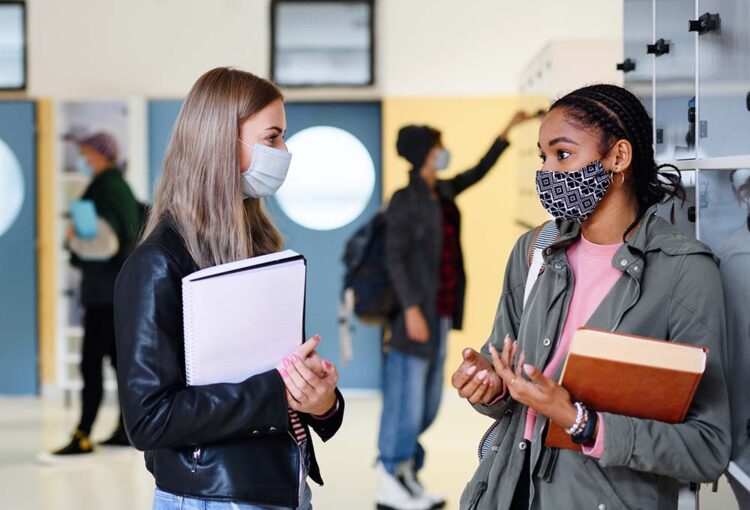 Two students wearing masks chatting in a high school hallway