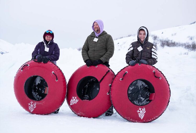 Two staff and a client standing with sledding innertubes outside in the snow