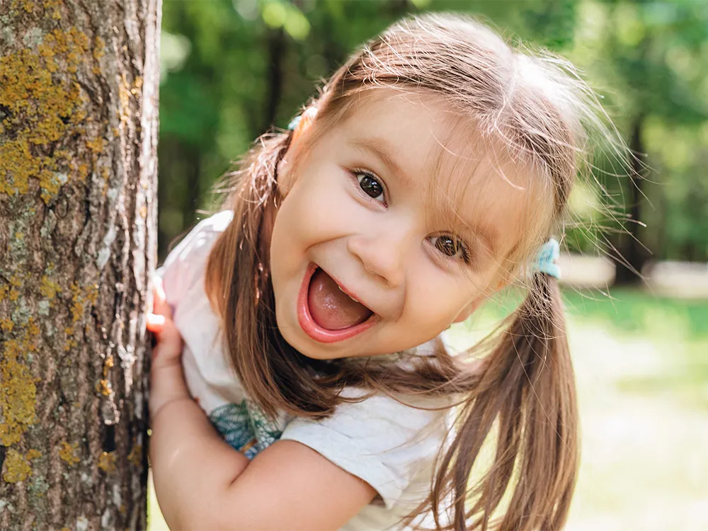Child leaning on tree towards camera and laughing