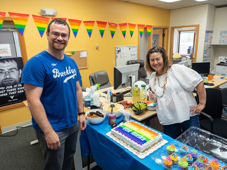 Two people smiling over a cake decorated for Pride month