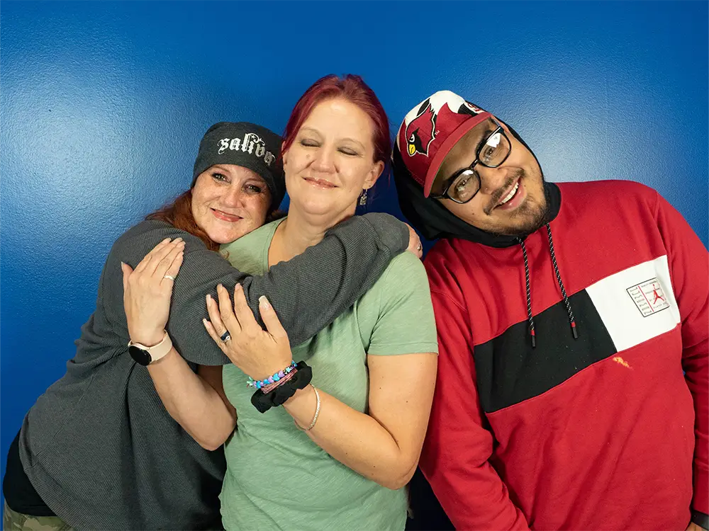 Two people hugging and another leaning on the shoulder of the middle person