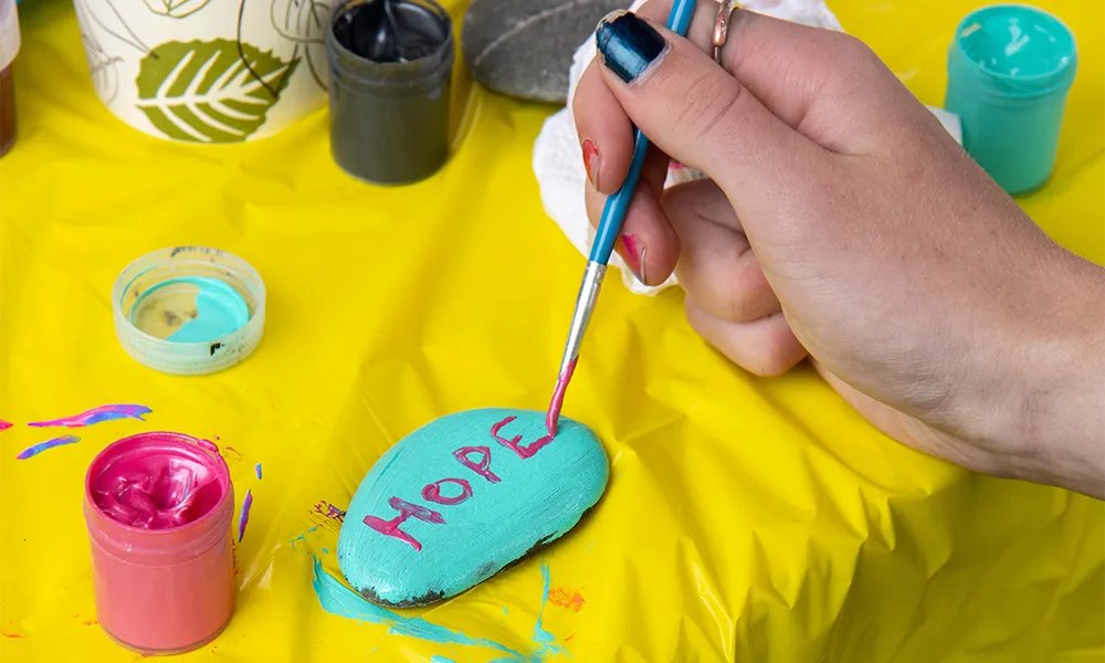 Young person painting the word HOPE on a rock with pink paint