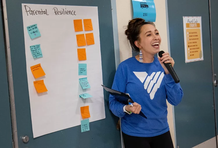 Person with VOA logo shirt speaking in microphone next to a large sheet of paper with "parental resilience" written and sticky notes below