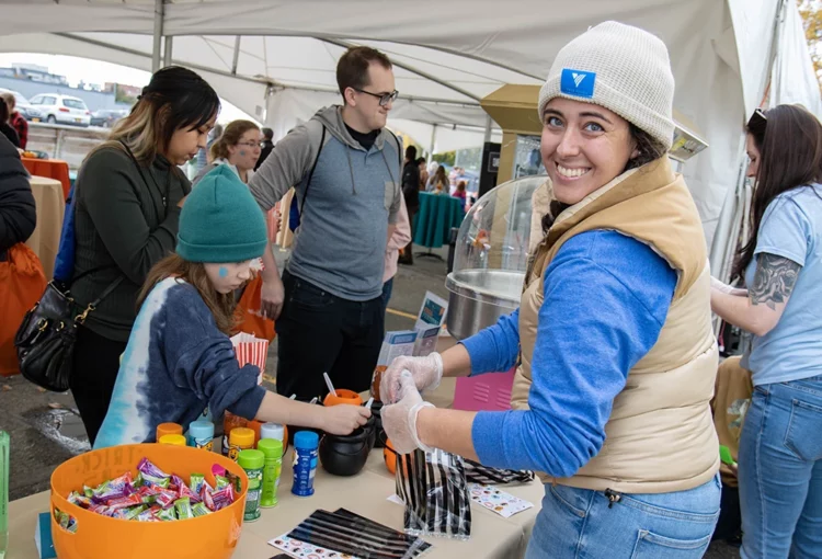 Staff member smiles at camera as she works a candy and popcorn table during a festival