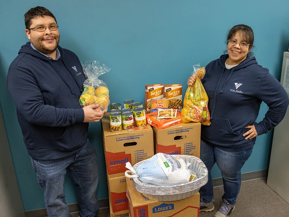 Two people posing with Thanksgiving meal donations - potatoes, turkey, canned goods