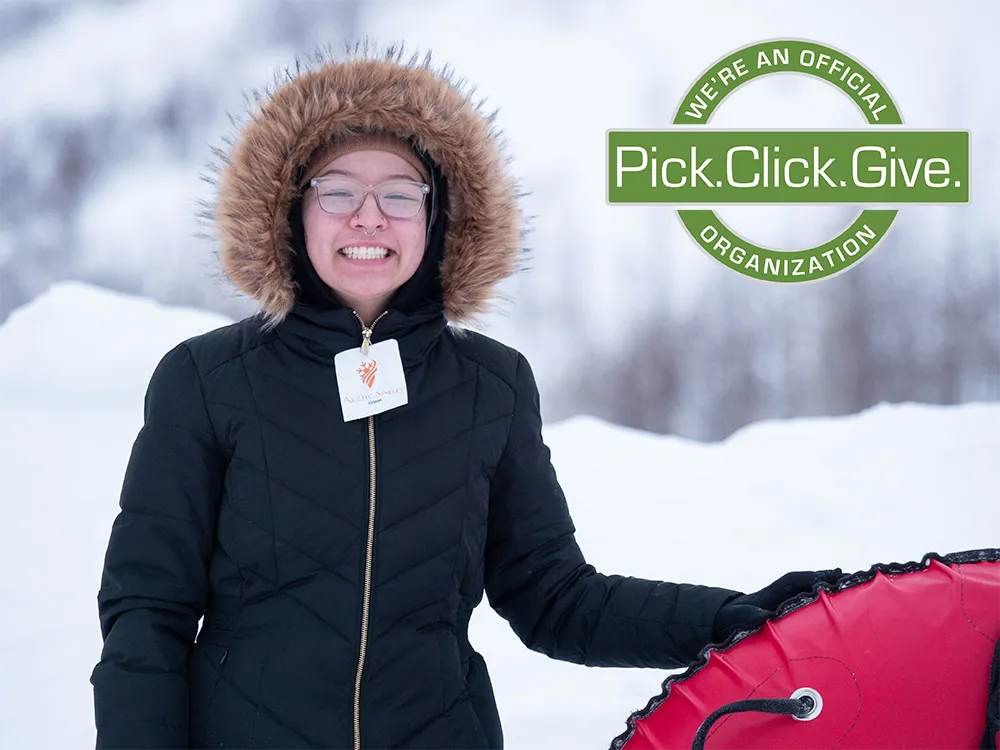 Teen smiling, dressing in winter jacket standing next to a giant sledding innertube.