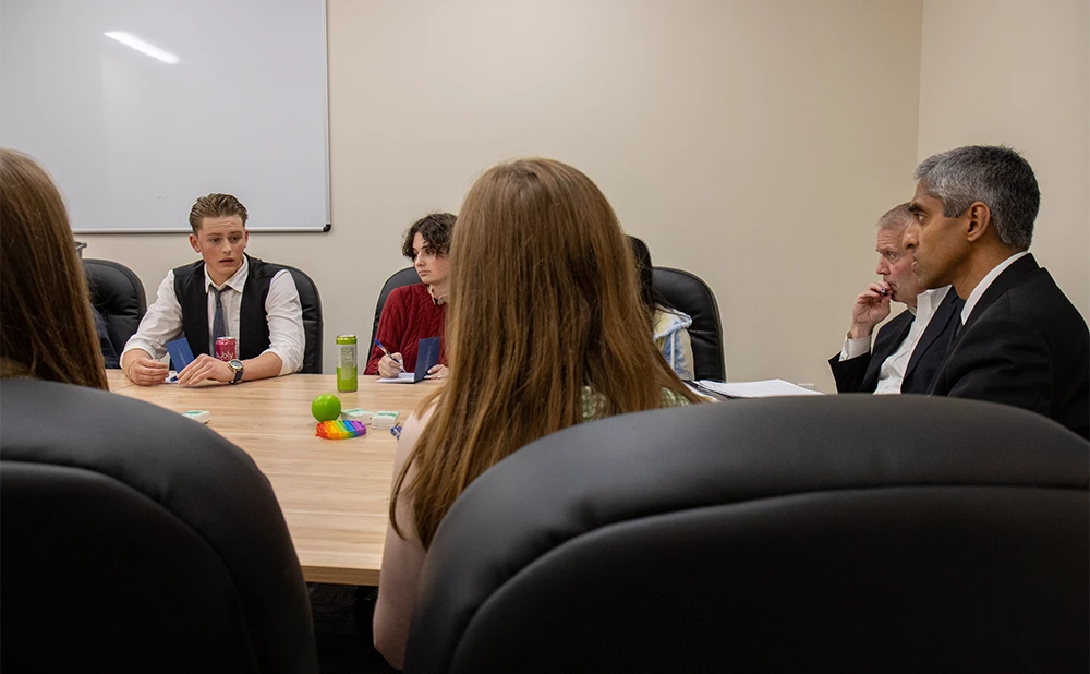 Youth sitting in a conference room, one is speaking while two adults listen intently.