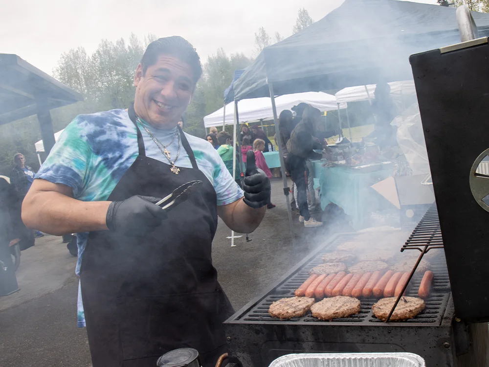 Person standing at a smoky open barbecue giving a thumbs up
