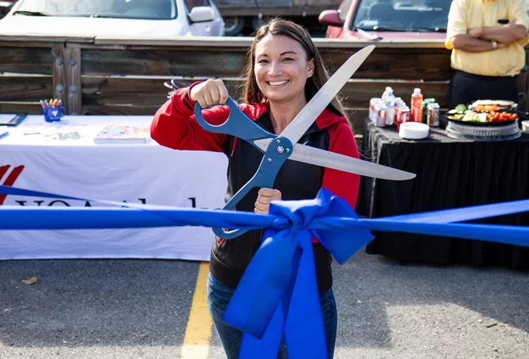 Woman holding giant scissors behind a blue ribbon