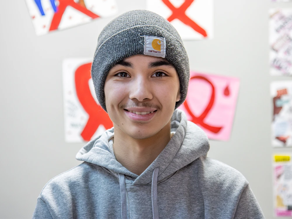A portrait of a teen, smiling, wearing a gray hoodie and beanie.