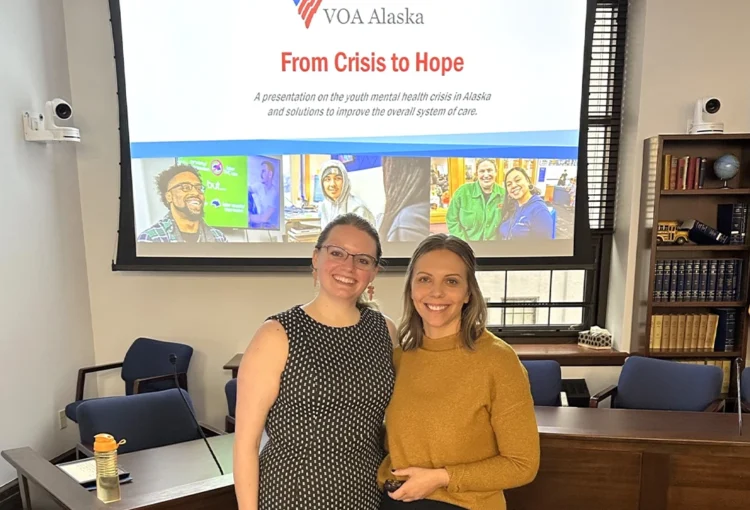 Two people standing in front of project screen, which shows a powerpoint slide titled: From Crisis to Hope.