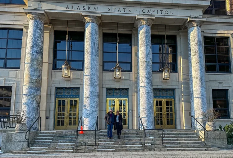 Two people standing on the steps of the Alaska State Capitol.
