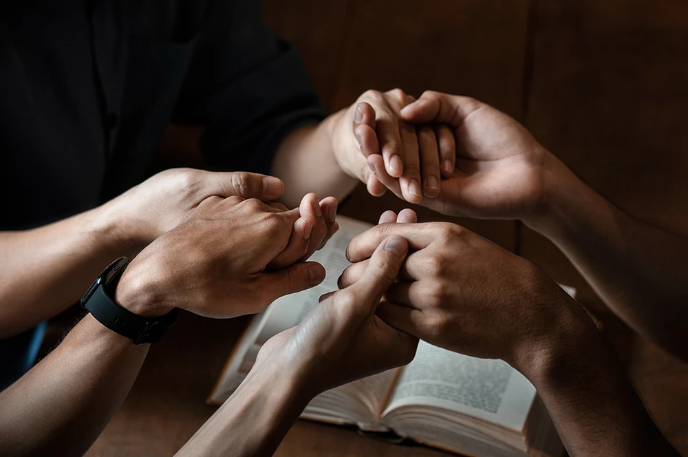 Close-up photo of hands praying over an open Bible.