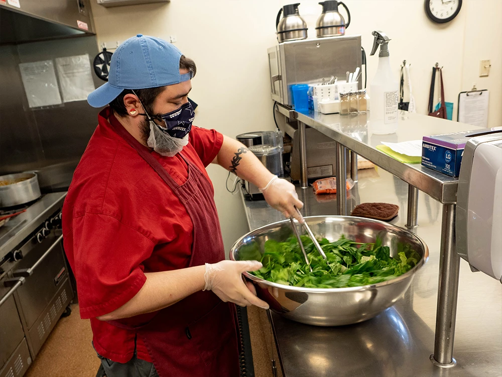 A kitchen worker tosses a salad with tongs.