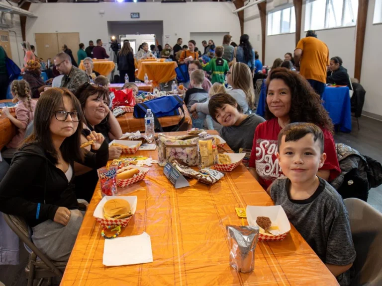 Wide shot of the room VOA Alaska's Fall Festival was held. In the image, you see attendees around tables and a projection of the Fall Festival logo on the wall.